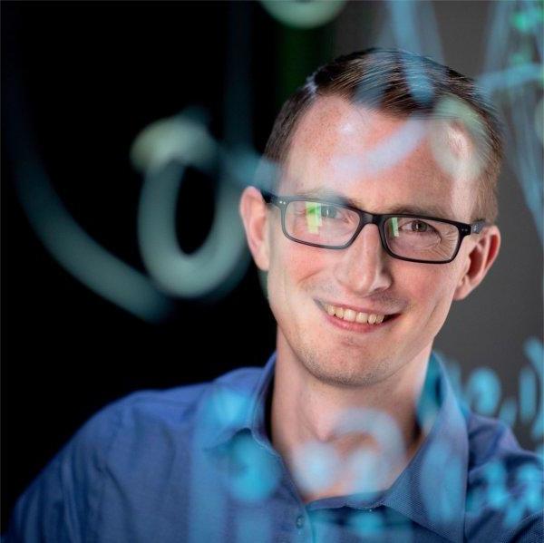 Zachary DeBruine in blue shirt behind screen with coding written on it